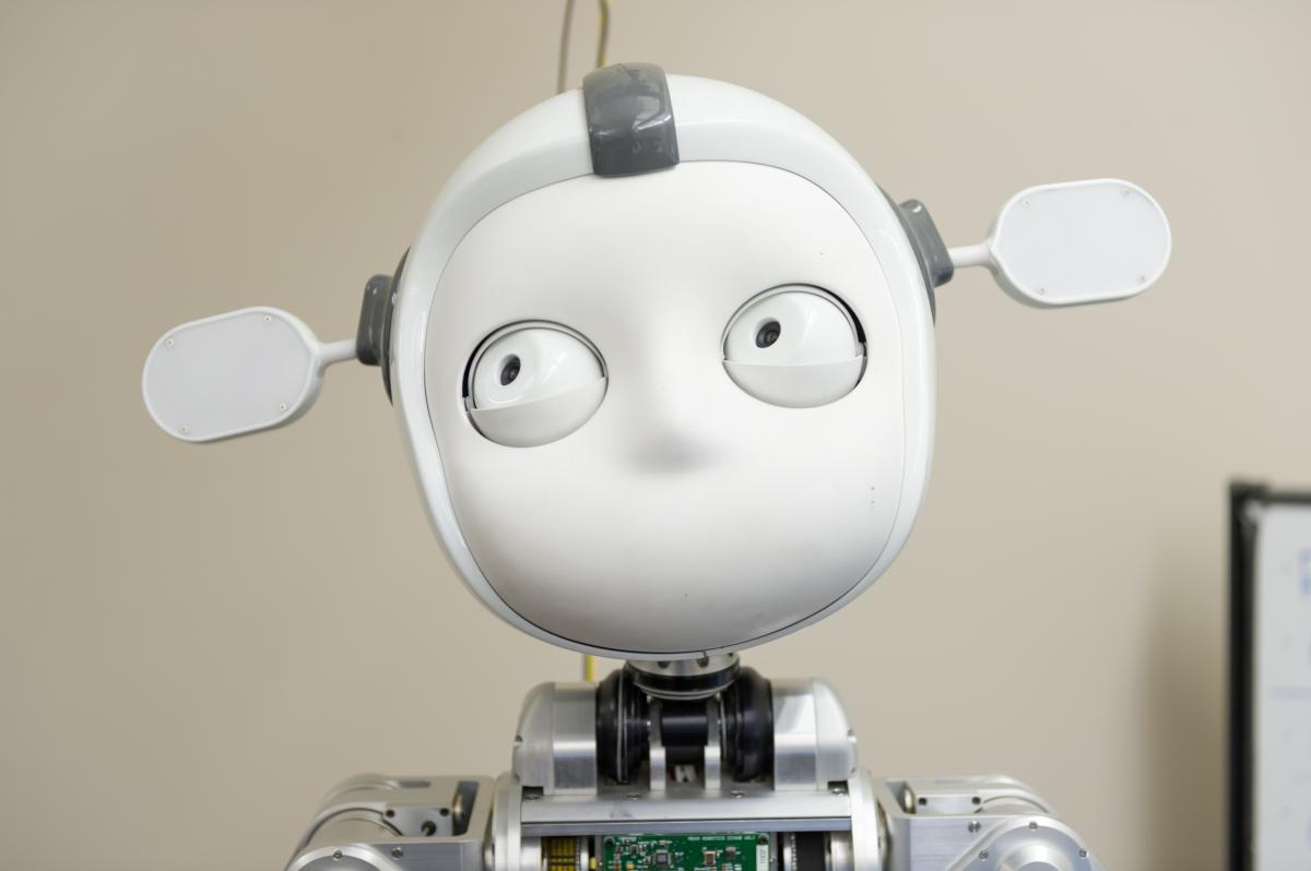 A light-colored robot with a human-like face, viewed from front, eyes pointing up and to the left.