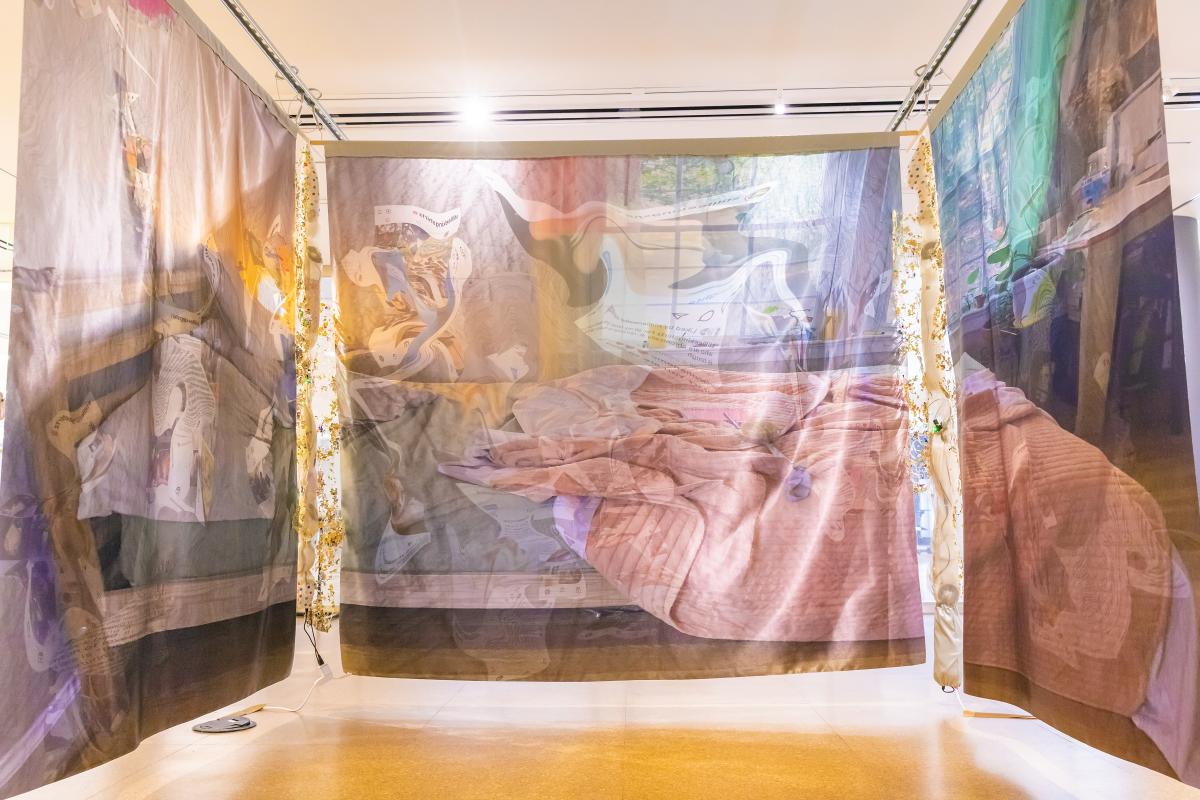 A view of the artist sleeping space, as seen from three tapestries. Phased in the image is digital distractions like social media feeds.
